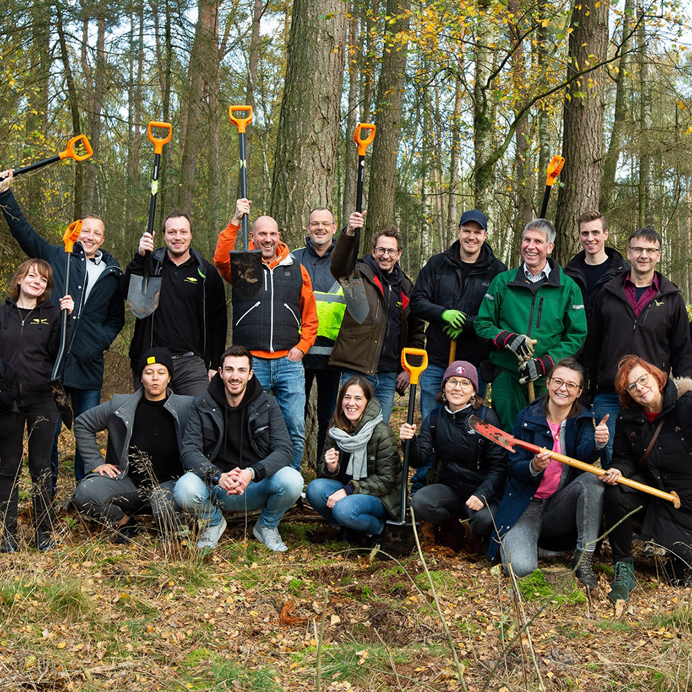 Eine Menschengruppe steht in einem Wald mit Schaufeln in den Händen