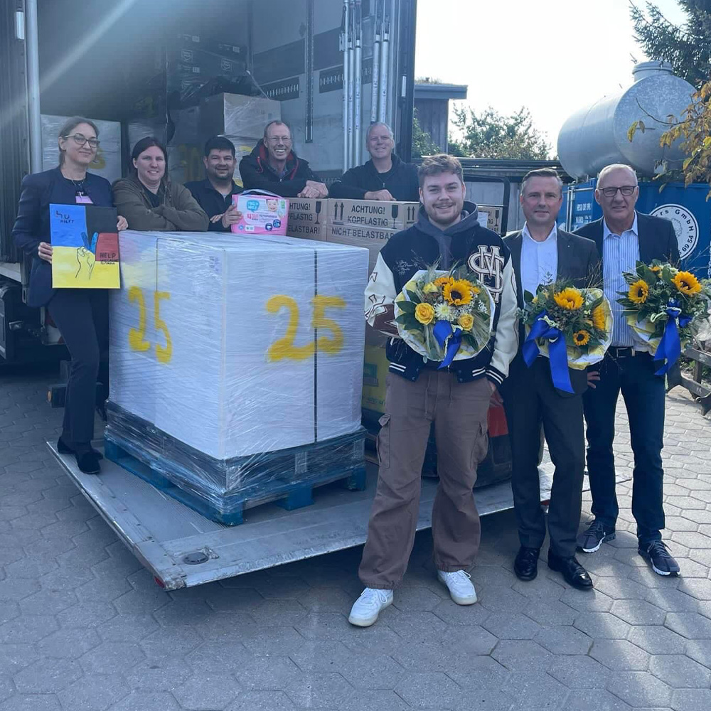 Eine Menschengruppe vor einem LKW mit Blumensträußen und Schildern