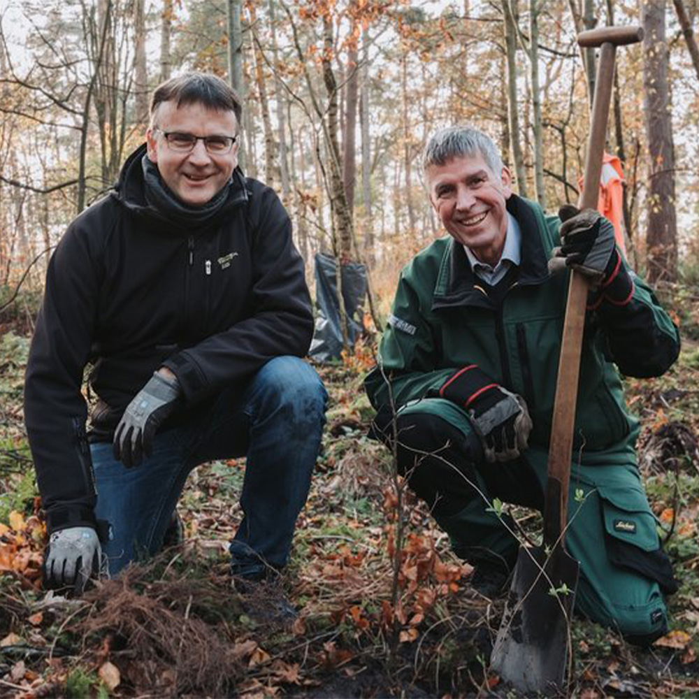 Zwei Männer knien im Wald mit lächelndem Blick in die Kamera