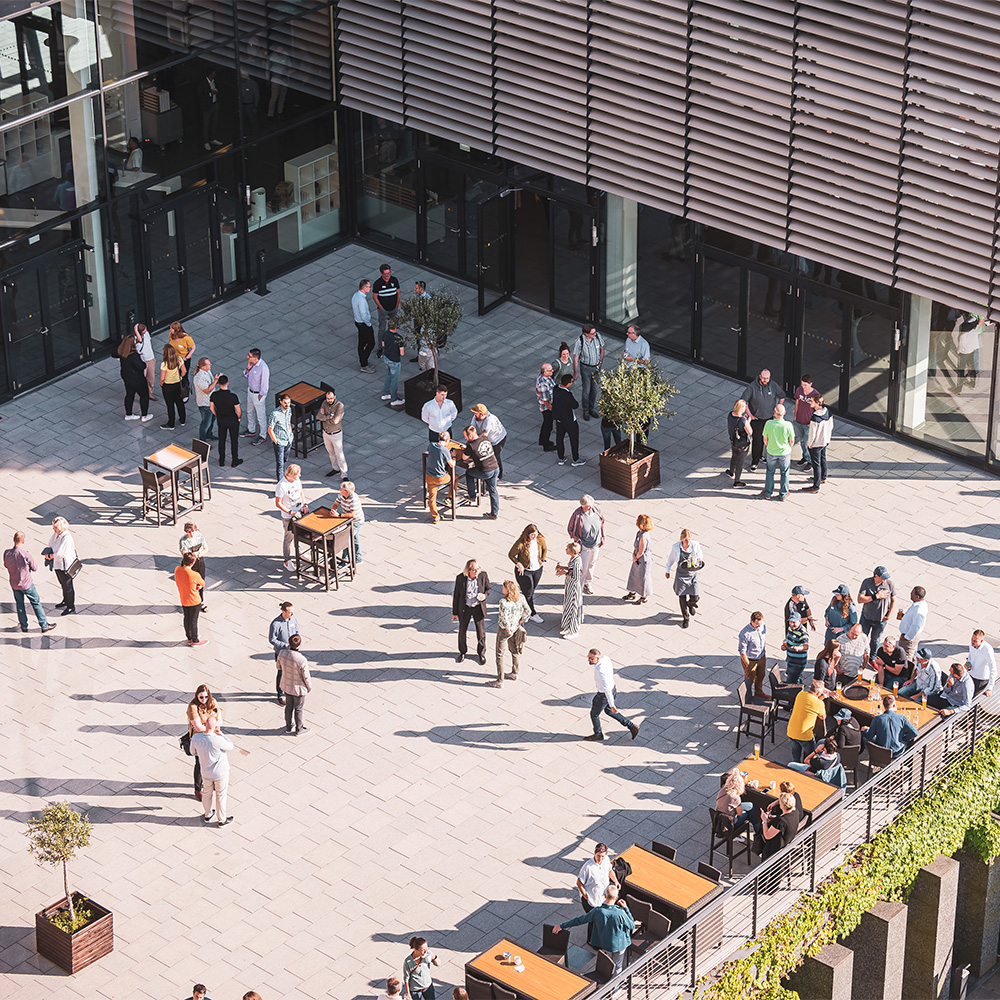 Menschen stehen und sitzen verteilt auf einem Platz vor einem Gebäude