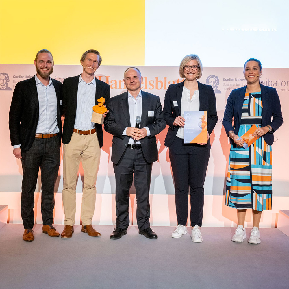 Fünf Personen stehen auf einer Bühne mit Trophäen und einer Urkunde